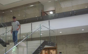 a person standing in a room with a staircase with glass railings